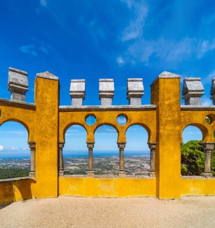 Moorish arches of the arched courtyard with the yellow painted walls of the Pena Palace, one of the most beautiful castles in Europe, under a clear blue sky. Sintra. Portugal. Vertical banner.