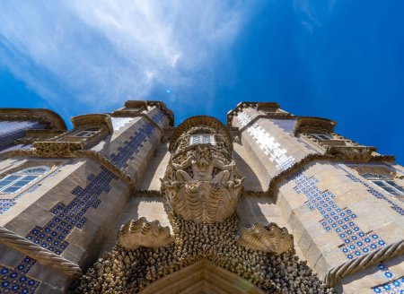 Vista en ángulo bajo de la Estatua de Tritón sobre un caparazón de piedra decorativa tallada que guarda la entrada al Palacio de Peña, con las torres decoradas con mosaicos portugueses. Sintra. Portugal.