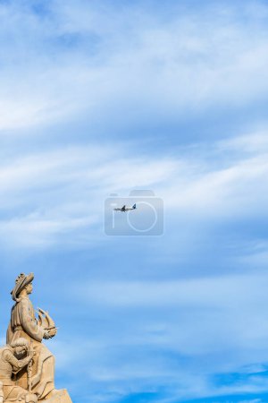 Monument der Entdeckungen aus Kalkstein: Heinrich der Navigator hält ein Schiff in der Hand, das in Richtung Amerika blickt, während ein Passagierflugzeug kopfüber vorbeifliegt, um Lissabon zu landen.