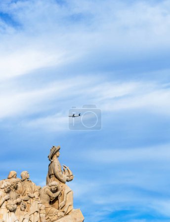 Foto de Monumento de piedra caliza a los descubrimientos, con Enrique el Navegante sosteniendo un barco mirando hacia las Américas con un avión de pasajeros pasando por encima de la cabeza para aterrizar en Lisboa. - Imagen libre de derechos