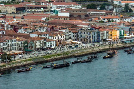 Widok z lotu ptaka na rzekę Douro i promenadę Porto ze starymi domami, rabelami, klasycznymi łodziami na szlaki turystyczne 6 mostów, restauracji i turystów spacerujących wzdłuż rzeki