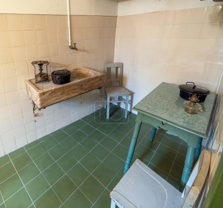 An old kitchen with sink from an old classic house from the 19th century with classic wooden furniture, green tiled floor, green table and marble sink with antique stove.
