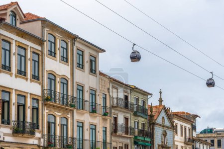 Two gondolas of the Gaia cable car passing just above typical houses in the Vila Nova de Gaia neighborhood, under a cloudy sky in Porto. Portugal.