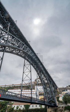Téléchargez les photos : Vue en angle bas du pont en acier Don Luis I à Porto et des personnes marchant et prenant des photos du fleuve Douro sur la plate-forme supérieure avec des maisons du vieux quartier ci-dessous. - en image libre de droit