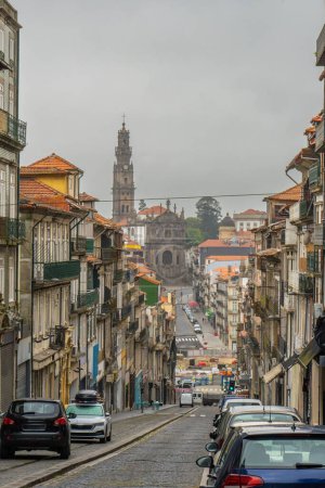 Foto de Empedrado calle turística de Oporto al amanecer, con el cielo nublado y la iglesia y la torre de Clerigos al final envuelto en una fina niebla. Portugal. - Imagen libre de derechos