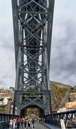 Téléchargez les photos : Touristes marchant le long de la plate-forme inférieure avec vue sur la structure métallique du pont en acier Don Luis I et la plate-forme supérieure à Porto avec des nuages de pluie. - en image libre de droit