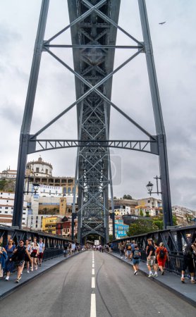 Photo for Tourists walking along the lower platform with a view of the metal structure of the Don Luis I steel bridge in Porto with rain clouds in the background. - Royalty Free Image