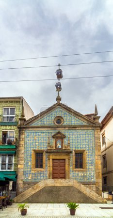 Two gondolas of the Gaia cable car passing just above the cross of the Chapel of Our Lady of Mercy forming a perpendicular line in Vila Nova de Gaia, decorated with tiles. Porto Portugal.