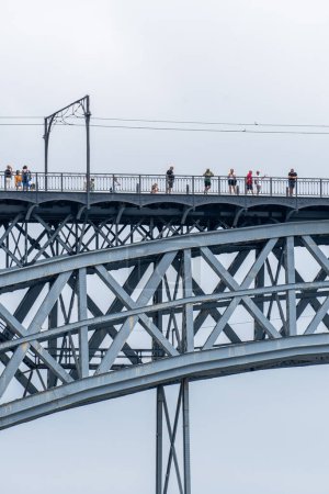 Téléchargez les photos : Pont en acier Don Luis I à Porto avec des nuages de pluie en arrière-plan avec des gens marchant et prenant des photos de la rivière Douro sur la plate-forme supérieure. - en image libre de droit