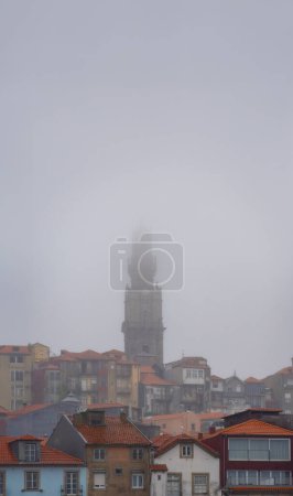 Church of the Clerics, baroque from the 17th century, standing out among the houses and roofs of the historic neighborhood of Porto, covered by fog and rain clouds on a romantic and bucolic gray day.