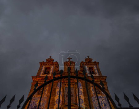 Front view from below of a spear-finish wrought iron fence of the Church of San Ildefonso decorated with Portuguese tiles illuminated beautifully under a gray and cloudy sky. Portugal.