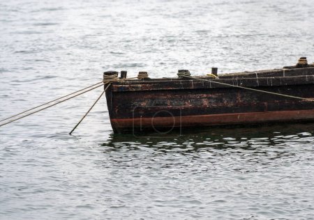 Small old wooden boat, docked with anchored ropes at the bottom of the Douro River on a very foggy day.