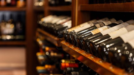 Téléchargez les photos : Bouteilles de vin rouge noir alignées, empilées et reposant en diagonale sur des étagères en bois dans un magasin de vin de collection de luxe. - en image libre de droit