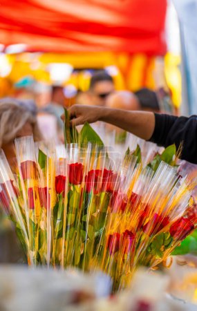 Florist's hand arranging a bouquet of roses at a flower and book stall in a traditional Catalan holiday market with many people walking and looking in the background on Sant Jordi's day.