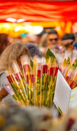 Ouvert livre blanc à côté d'un bouquet de roses à un stand de fleurs et de livres dans un marché de vacances catalan traditionnel avec beaucoup de gens qui marchent et regardent en arrière-plan le jour de Sant Jordi.