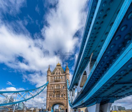 Blick von der Straße und in die Perspektive der Struktur und Zugseile der beleuchteten London Tower Bridge mit dem Stadtbild im Hintergrund.