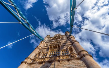 Vue d'en bas en perspective et plan nadir du Tower Bridge de Londres illuminé par le soleil et avec les ombres des câbles en acier sur sa façade par une journée ensoleillée avec des nuages blancs.