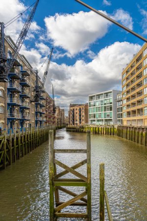 Ehemalige historische Lagerhallen, die jetzt in Wohnhäuser umgewandelt wurden, säumen die Themse wie ein Kanal mit grünem Schlamm und Moos bei Ebbe in den Docklands in London, England.