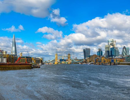 Panoramic view from the River Thames of the London skyline with the skyscrapers and Tower Bridge illuminated by the morning sun and the boats and ferries moored at its docks.