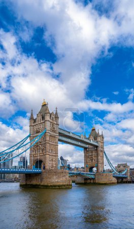 Diagonal view of London's Tower Bridge with its reflection in the River Thames under a blue sky with white clouds. United Kingdom.