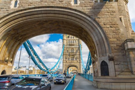 Vista a través del arco de una de las torres del Tower Bridge de Londres, con la vista de las estructuras en perspectiva y los turistas y coches circulando por la calle.