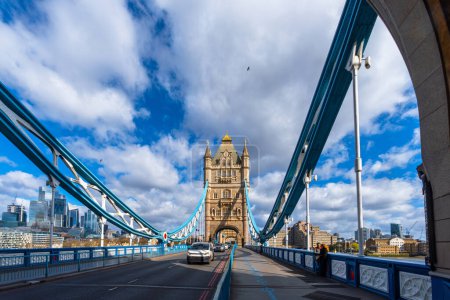Zwei Freunde unterhalten sich angelehnt am Zaun der inneren Promenade der Tower Bridge in London, mit Blick auf die Spannstrukturen der Brücke und Touristen und Autos, die die Straße entlang fahren.