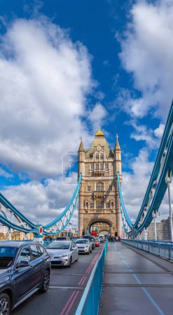 Autoverkehr und Touristen auf der Straße der Tower Bridge in London, mit Blick auf die Spannkonstruktionen der Brücke an einem Tag mit sonnigem blauen Himmel und weißen Wolken.