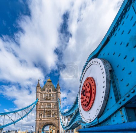 View from the street and in perspective of the structure with the red and white connections for the tension cables of the Tower Bridge of London with the urban landscape in the background.
