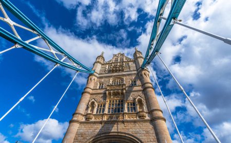 Vista desde abajo en perspectiva y plano nadir del Tower Bridge de Londres iluminado por el sol y con las sombras de los cables de acero en su fachada en un día soleado con nubes blancas.