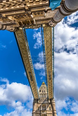 Blick von unten auf das Nadir der Tower Bridge, mit Blick auf die Korridore und die oberen Plattformen der Laufstege mit Glasplatten am Boden unter einem sonnigen Himmel mit weißen Wolken in London.
