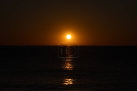 Die Morgensonne erhellt den dunklen Morgenhimmel und das Meer und die Silhouetten einer Gruppe von Fischerbooten, die entlang der Horizontlinie des Mittelmeeres segeln.