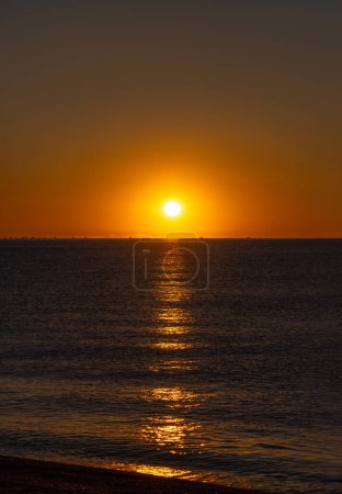 Ruhiges Meer im orangen Licht der hellen Morgensonne, die die Silhouetten einer Gruppe von Fischerbooten erhellt, die im Mittelmeer nach Palamos-Garnelen fischen.