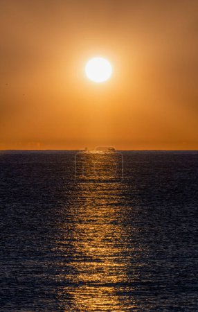 Ruhiges Meer im orangen Licht der hellen Morgensonne, die die Silhouetten zweier Gruppen von Fischerbooten erhellt, die im Mittelmeer nach Garnelen fischen.