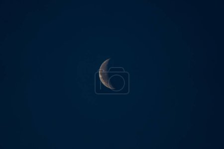 Perfectly detailed crescent moon with its craters and lunar seas on a dark blue dawn sky.