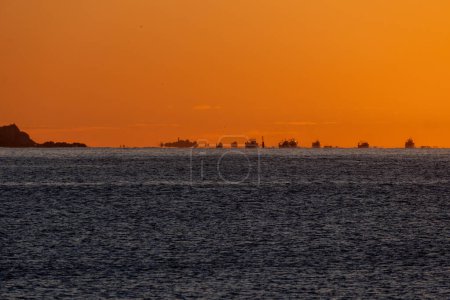 Fischerboote an der Horizontlinie des Mittelmeeres, die vom Hafen und von der Küste aus zum Garnelenfischen aufs Meer hinausfahren, beleuchtet von der Morgensonne, die Fata Morgana und optische Täuschungen erzeugt.