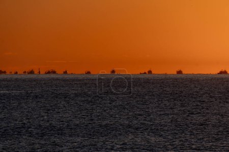 Siluetas de un grupo de barcos de pesca en el momento de la salida al mar para pescar los camarones, iluminados por el sol del amanecer en la línea del horizonte del mar Mediterráneo, creando espejismos.