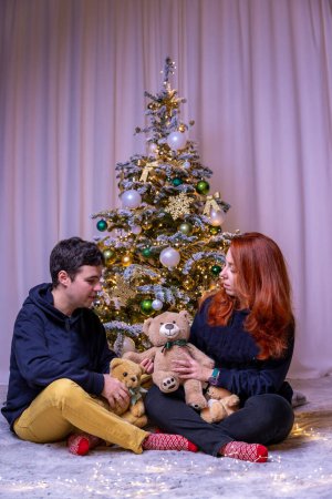 Photo for A married couple with a red-haired girl are sitting under a decorated Christmas tree and looking at soft toys. High quality photo - Royalty Free Image