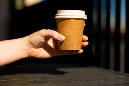 Photo for A womans hand holds a paper cup of coffee with a white lid. Summer, sunny day. High quality photo - Royalty Free Image