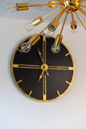 Photo for An unusual lamp incandescent lamps against background large wall clock Beautiful high-tech chandelier. High quality photo - Royalty Free Image