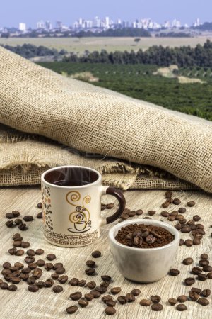 A Cup of fresh coffee and roasted beans in a bag and pot on the table against the backdrop of a coffee plantations and skyline city in Brazil