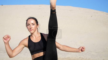 Photo for Portrait, athletic girl in a black top, athlete, practice kicks, kicks feet in front of the camera. On a deserted beach, in the summer, under a hot sun. Slow motion. High quality photo - Royalty Free Image