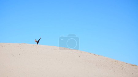 Photo for Athletic girl in black , practice lifting of the legs, fulfills the kicks, fight with the shadow, training to fight. On a deserted beach, against a blue sky, in the summer, under a hot sun. High - Royalty Free Image