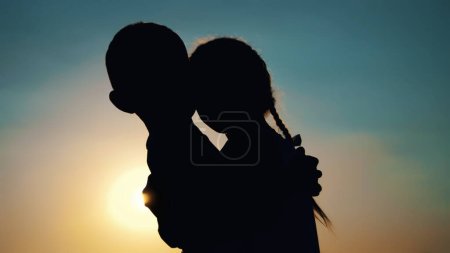 Foto de Siluetas, figuras de niños, niño y niña, hermano y hermana abrazándose contra el fondo del sol, al atardecer, en verano. Foto de alta calidad - Imagen libre de derechos