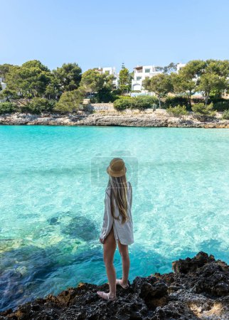 Photo for Rear view of standing woman with long blonde hair in cala pi, Mallorca, balearic islands. Turquoise water rounded by rocks - Royalty Free Image