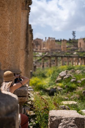 Téléchargez les photos : Vue arrière du chapeau femme touriste blonde prenant une photo dans les ruines de l'ancien Jerash, Jordanie - en image libre de droit