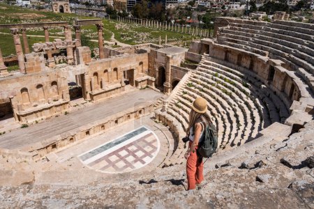 Téléchargez les photos : Voyage touristique femme blonde avec chapeau et sac à dos dans le théâtre romain à Jerash, Ancienne ville romaine en Jordanie - en image libre de droit