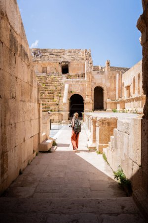 Téléchargez les photos : Vue arrière de la femme blonde touristique avec chapeau, sac à dos et caméra dans les ruines de l'ancien Jerash, Jordanie - en image libre de droit