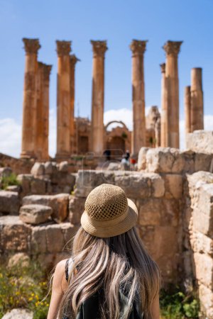 Téléchargez les photos : Vue arrière de la femme touristique blonde avec chapeau dans les colonnes du temple de Zeus, Jerash, ancienne ville romaine de Gerasa - en image libre de droit