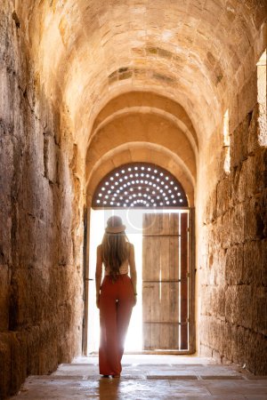Téléchargez les photos : Vue arrière de la femme blonde avec chapeau devant la porte d'entrée Ruines Jerash antiques, Jordanie - en image libre de droit