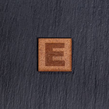 Photo for Capital Letter In Square Wooden Tiles - Letter E, On Black Stone Background. - Royalty Free Image